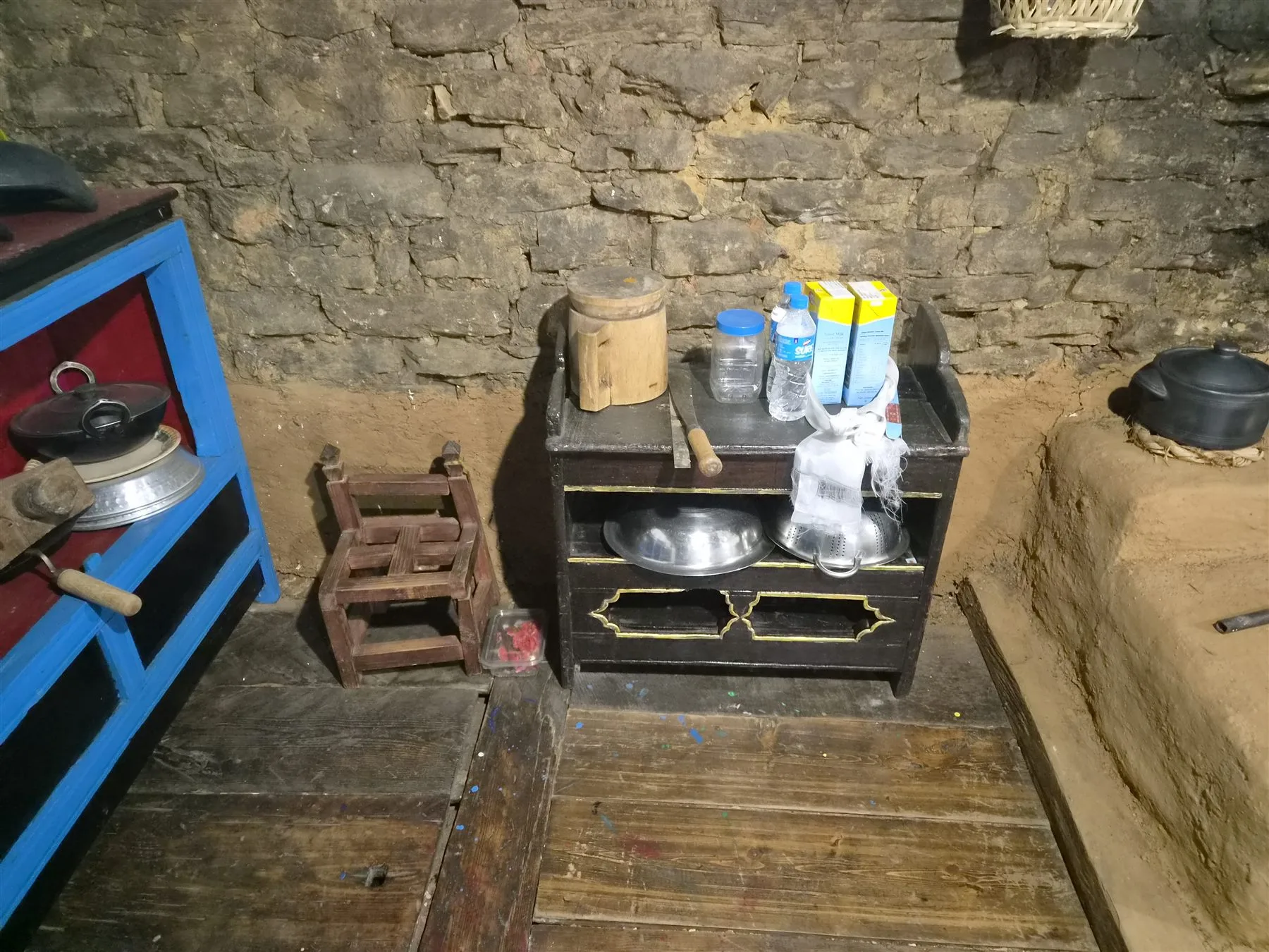 Wooden kitchen tools beside a stone wall and clay hearth